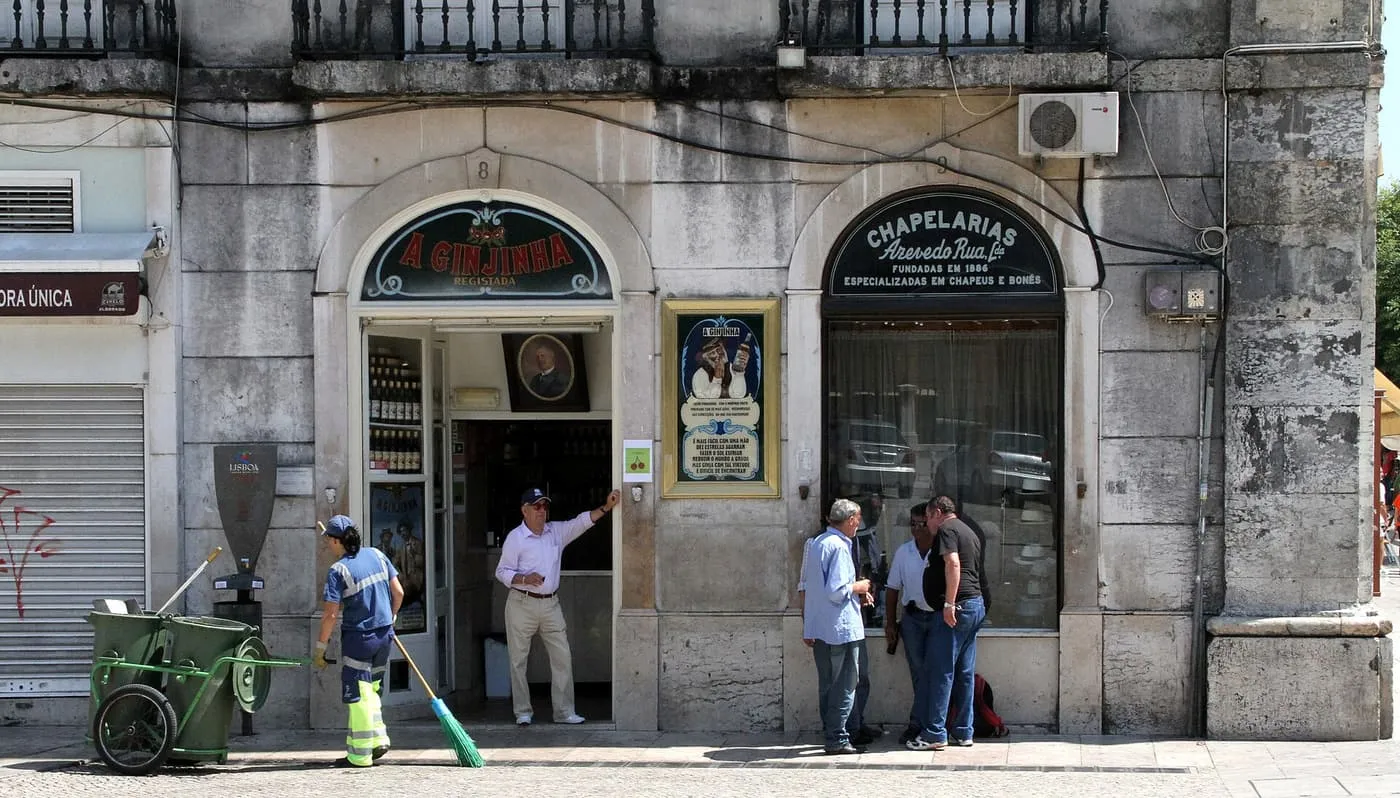 The arched shopfront of A Ginjinha, the cherry-liqueur bar by Rossio, with a man in the doorway and passers-by on the pavement
