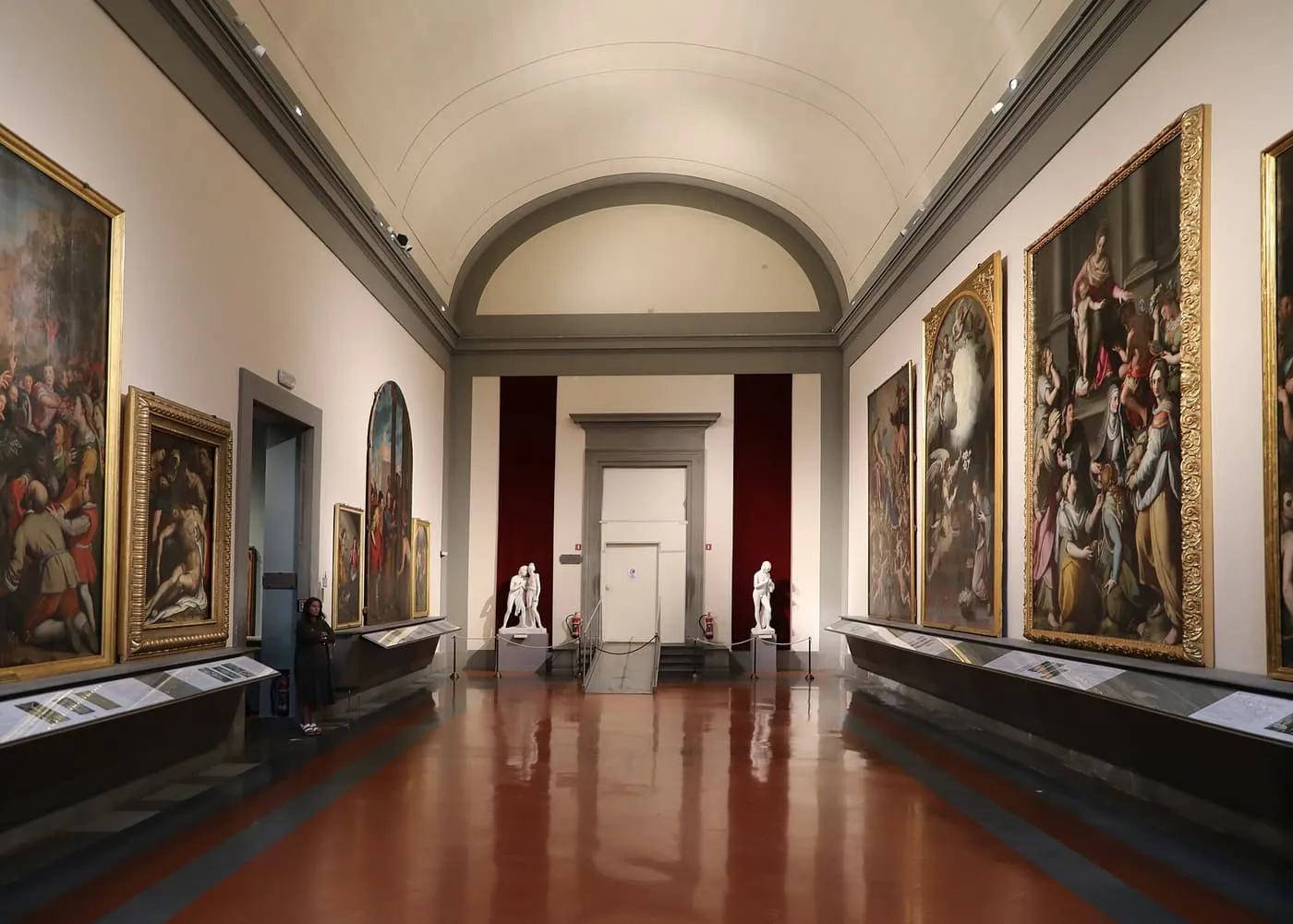 A long vaulted gallery in the Galleria dell'Accademia hung with large altarpieces, with two white marble statues at the far end