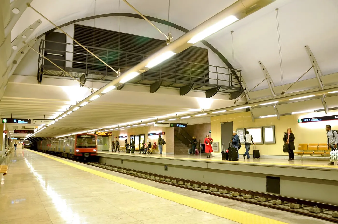 A red Metro train pulling into Aeroporto station, with passengers and their suitcases waiting on the platform
