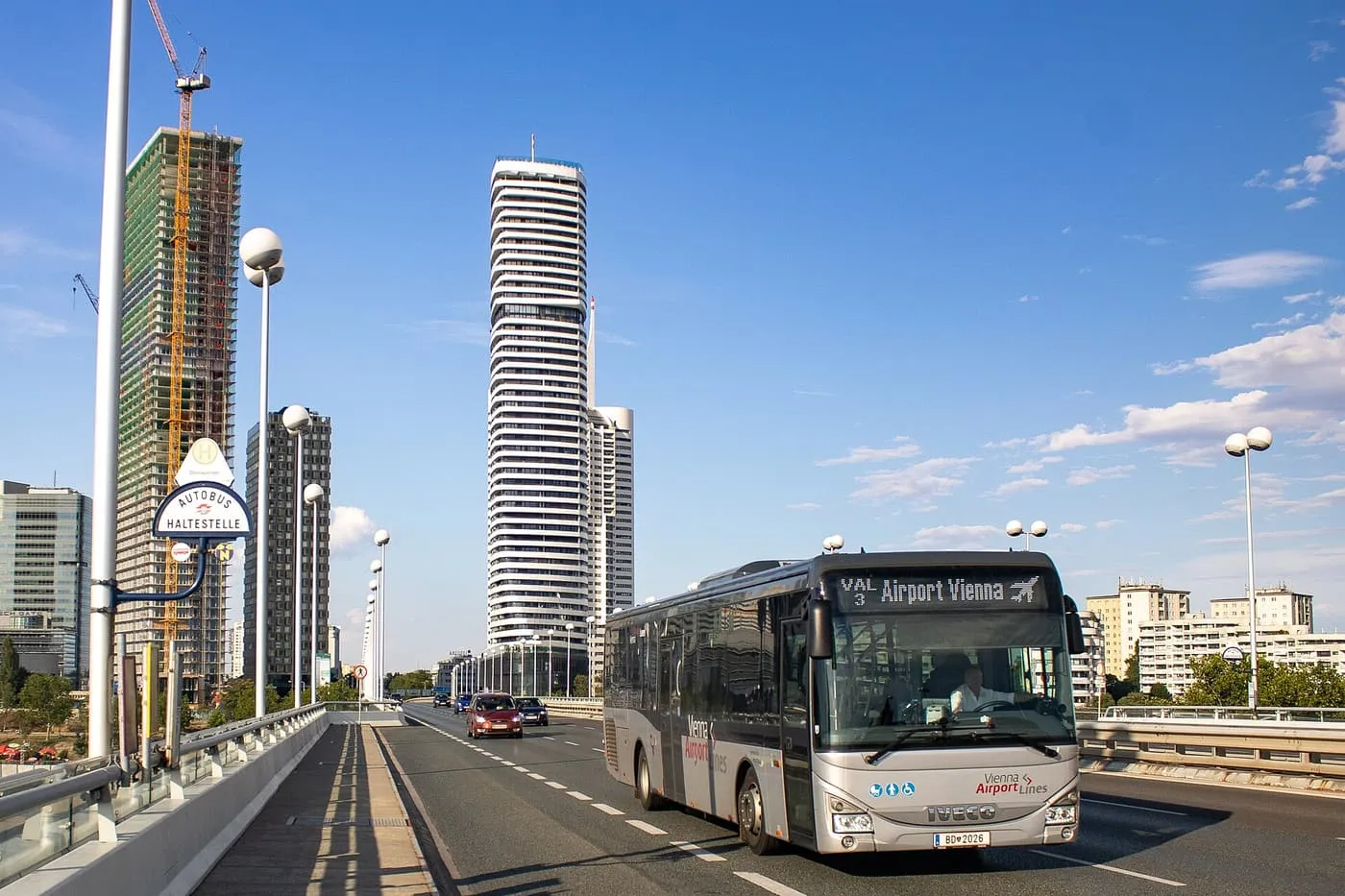 A silver Vienna Airport Lines bus crossing the Reichsbrücke with high-rise towers behind