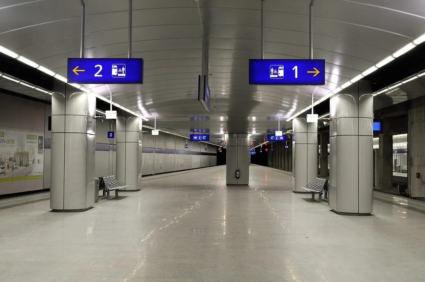 Two empty platforms at Vienna Airport station under a curved ceiling, with blue platform signs