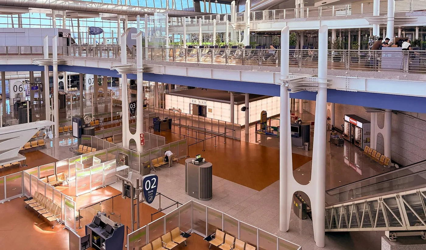 The gate area inside Porto airport terminal, seen from an upper gallery, with white columns, gate desks and rows of seats