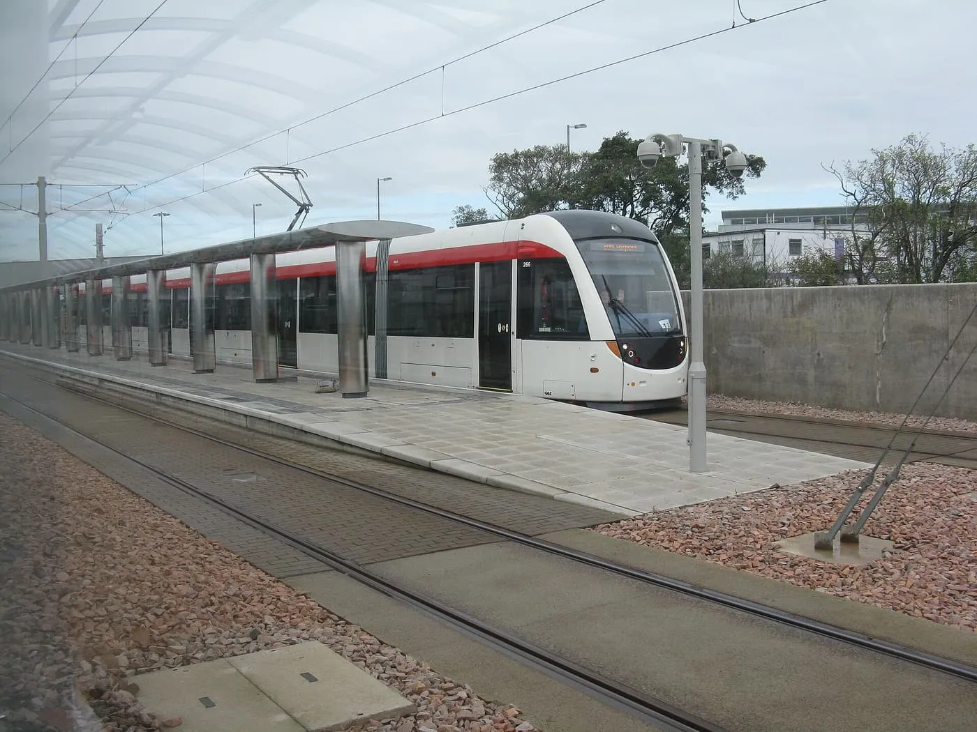 A white and red Edinburgh tram standing at the covered platform of the airport tram stop