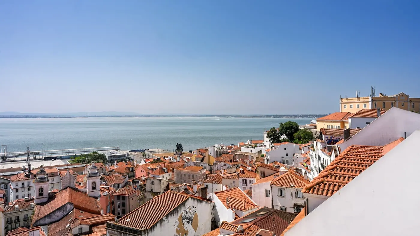 Red-tiled roofs of Alfama running down to the Tagus under a clear sky