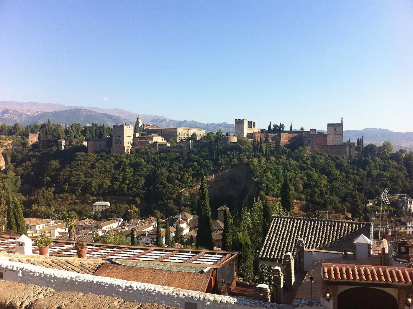 The Alhambra on its wooded hill above the rooftops of the Albaicín, with mountains beyond