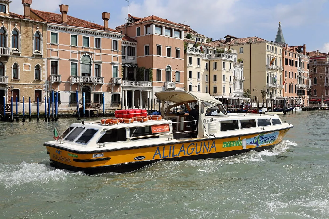 A yellow and white Alilaguna boat on the Grand Canal in front of palaces
