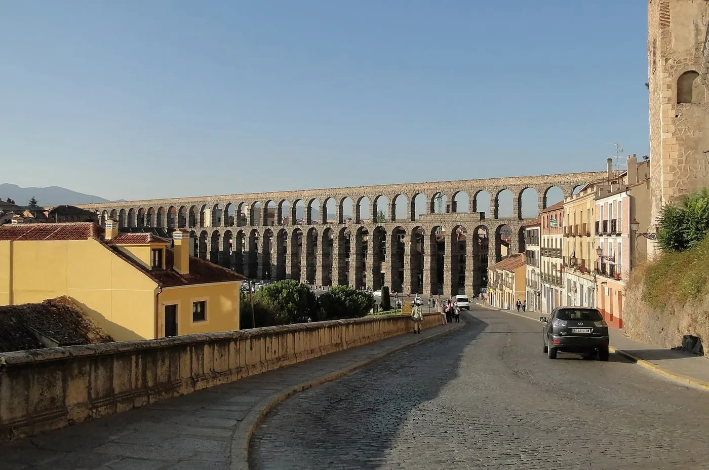 The Roman aqueduct of Segovia running across the old town on two tiers of granite arches, seen from a cobbled street