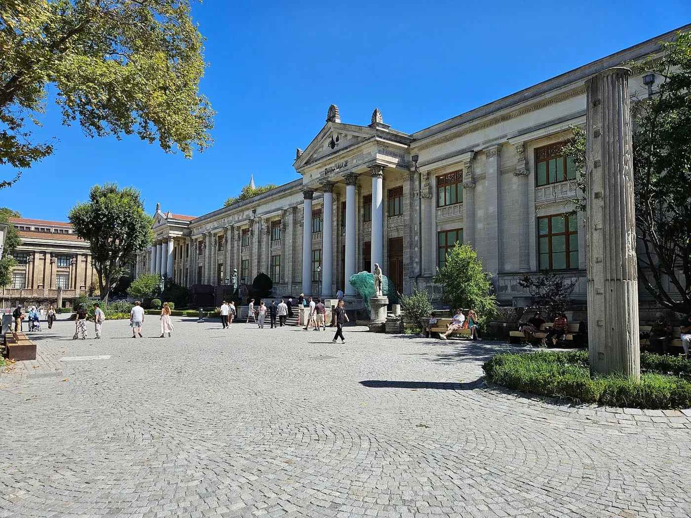 The columned front of the Istanbul Archaeology Museums across a paved courtyard, with visitors walking towards it