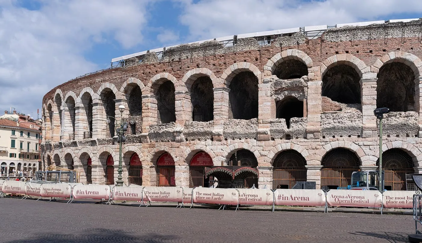 The curved outer wall of Verona's Roman Arena, with tiers of stone arches rising from the cobbled square