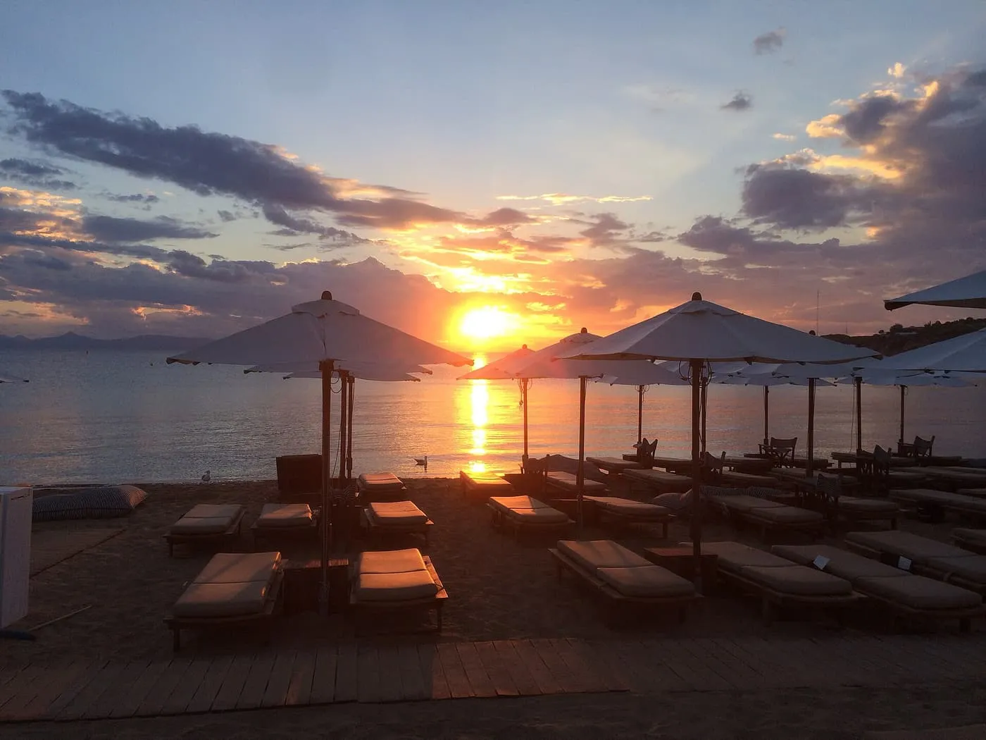 Sun loungers and white parasols on the sand at Astir Beach in Vouliagmeni, with the sun setting over the sea