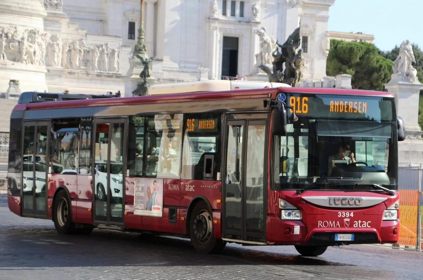 A red ATAC bus on route 916 crossing a cobbled square, with the white Vittoriano monument behind