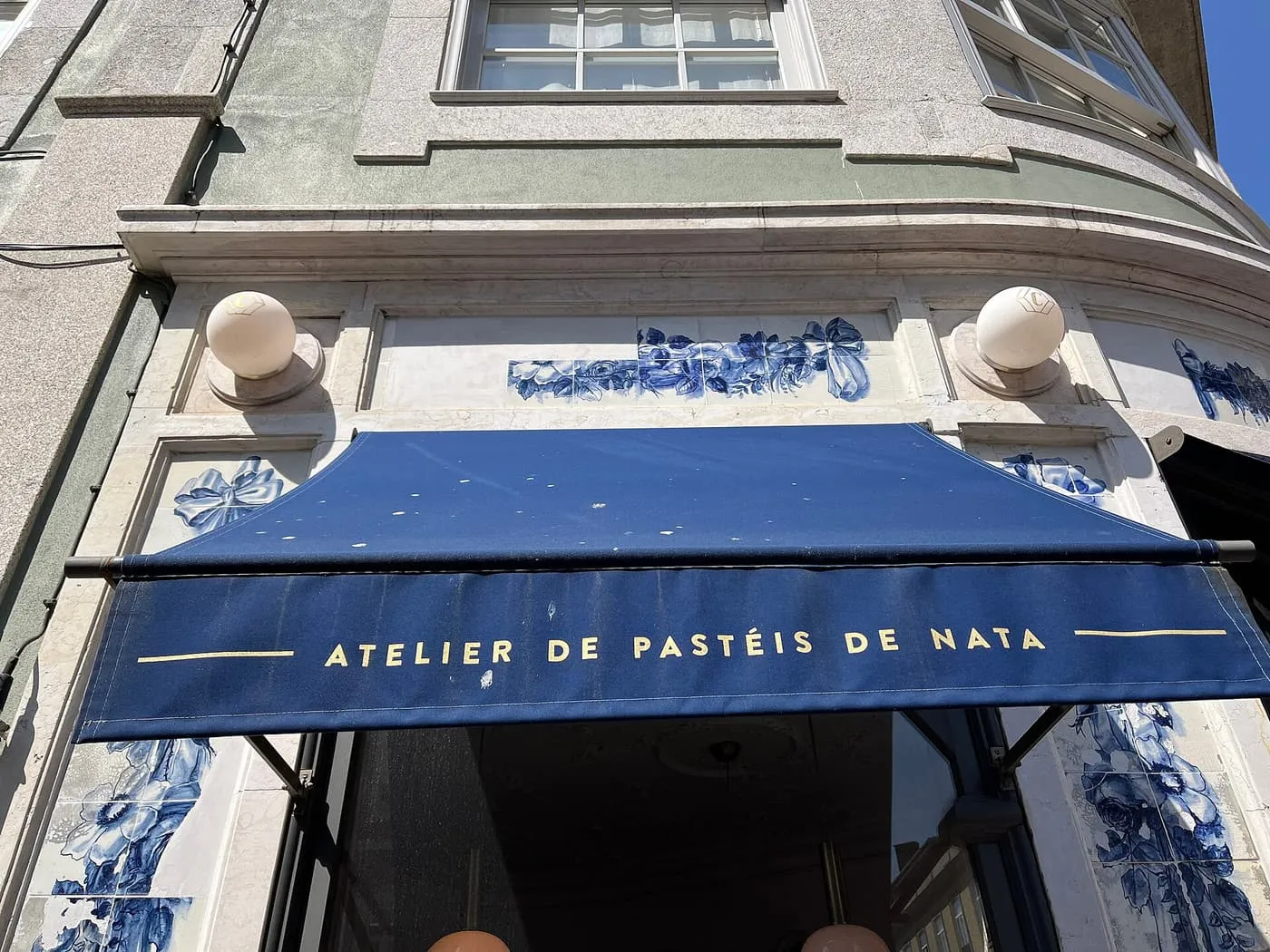 A navy awning reading Atelier de Pastéis de Nata over a doorway framed in blue-and-white tiles
