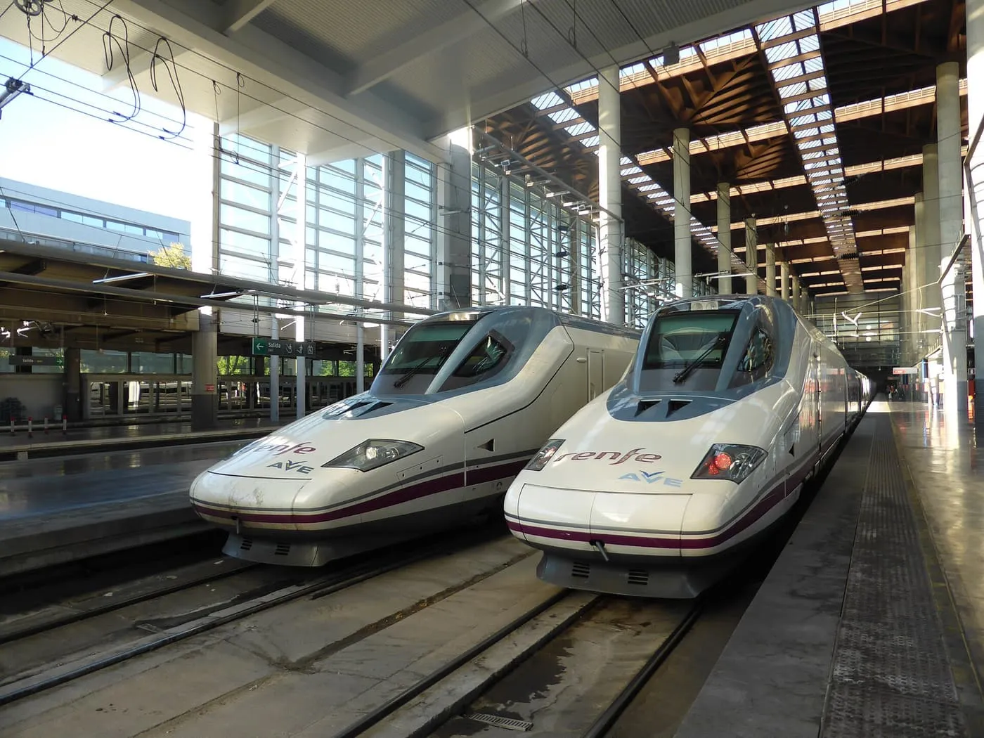 Two white Renfe AVE high-speed trains with purple stripes side by side at a platform of Madrid Puerta de Atocha station