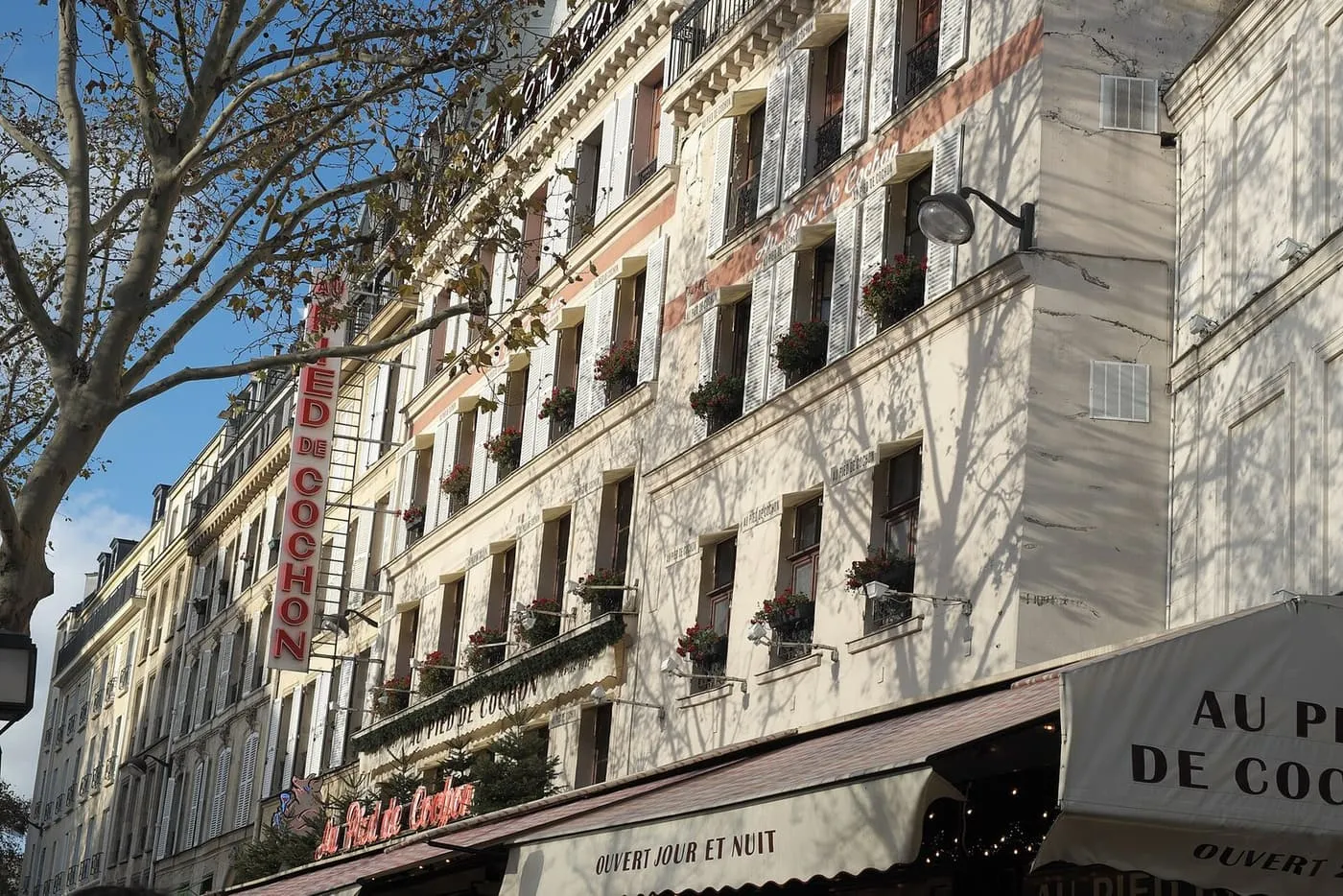 The white corner building at 6 rue Coquillière with the red awning and lettering of Au Pied de Cochon, and its tall vertical sign