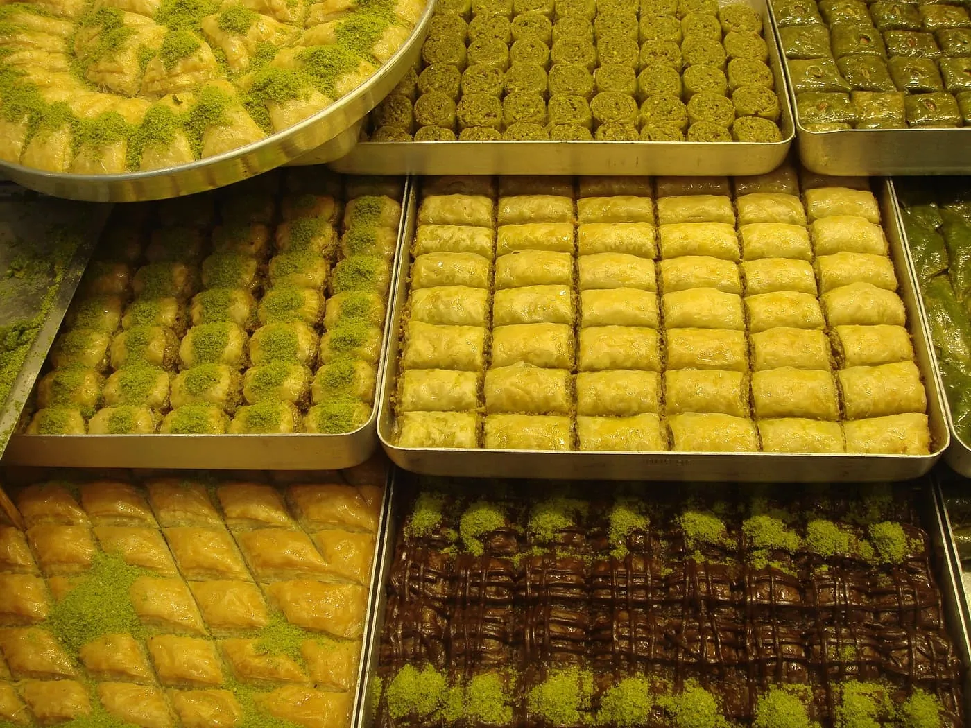 Trays of baklava in a shop window, some cut in diamonds and sprinkled with ground pistachio