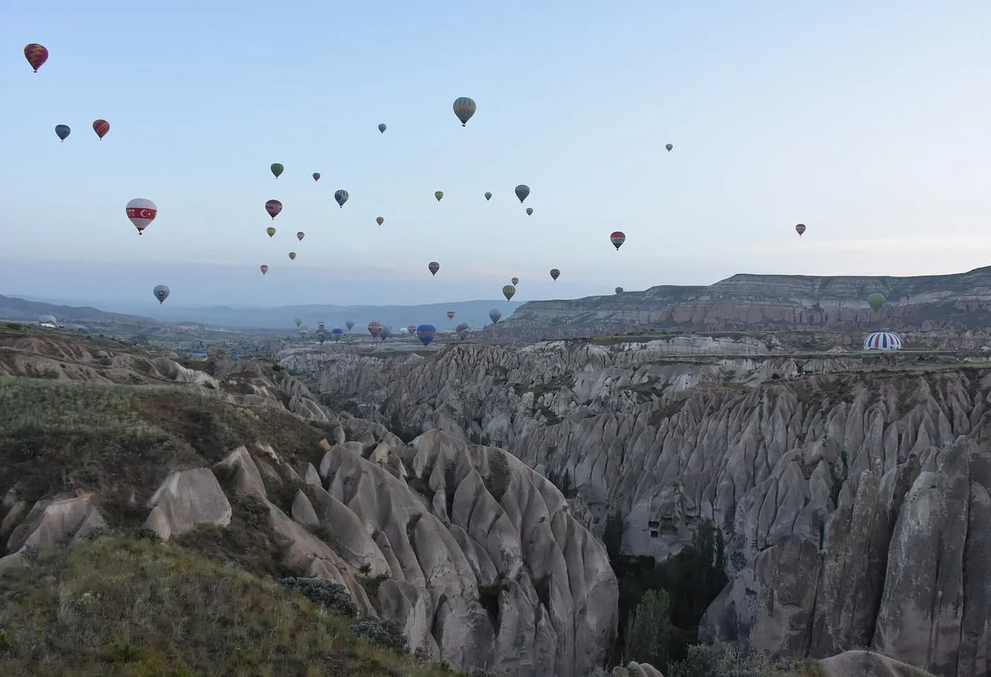 Dozens of hot air balloons floating at dawn over the grey rock ridges and valleys near Göreme
