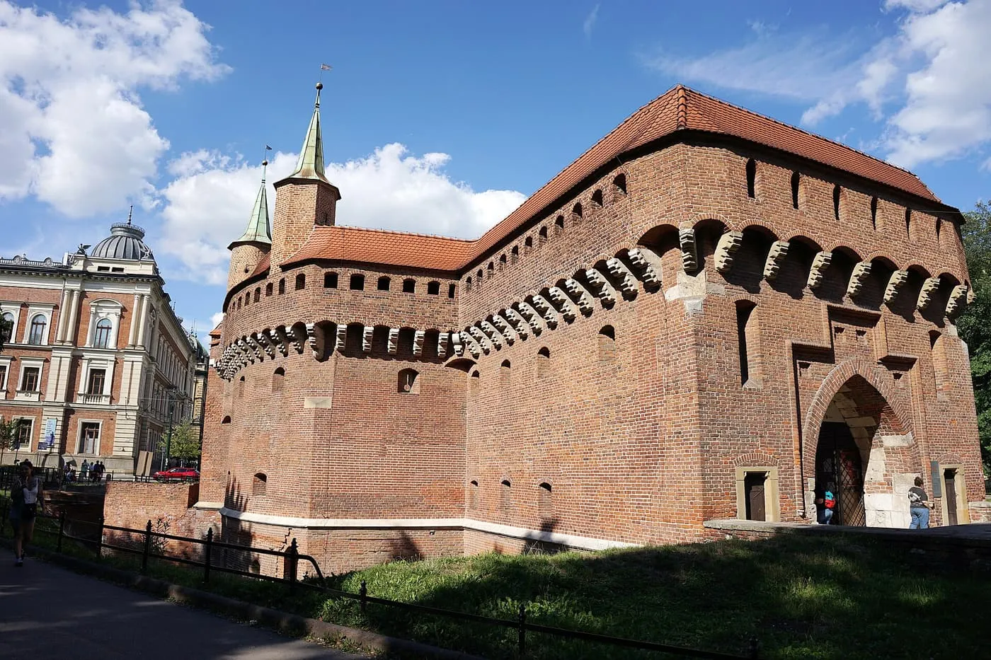 The Barbican, a round brick fortress with turrets and a red tiled roof, behind a lawn and railings