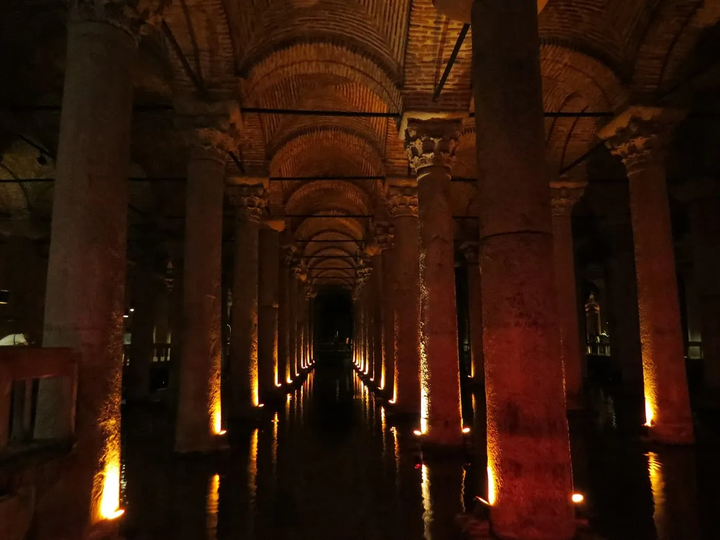 Rows of floodlit stone columns and brick vaults receding into the dark water of the Basilica Cistern