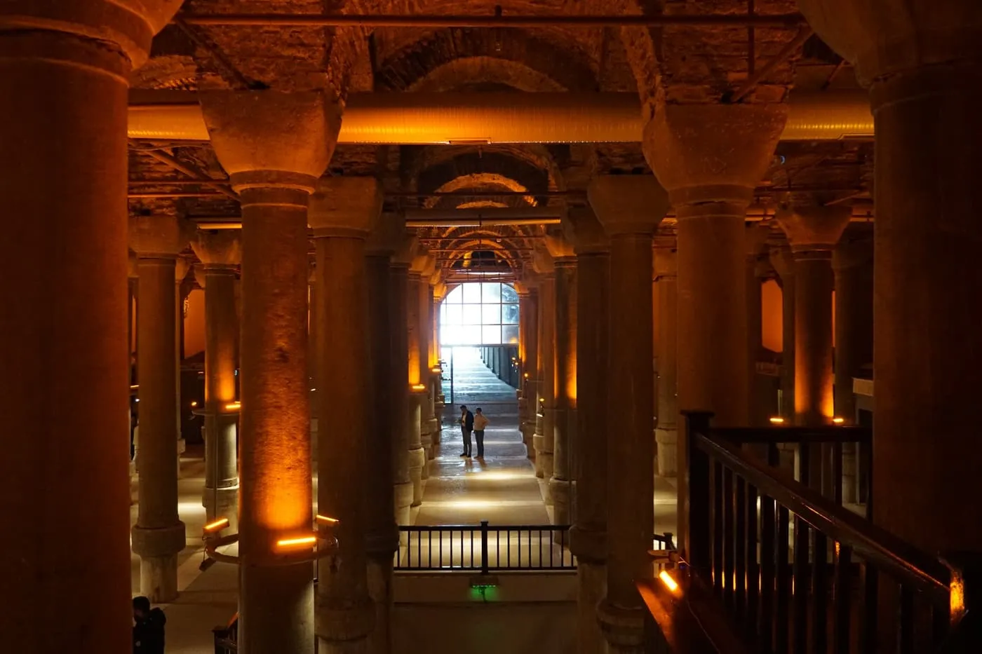 Rows of stone columns lit in amber in the Basilica Cistern, with daylight at the far end of the walkway