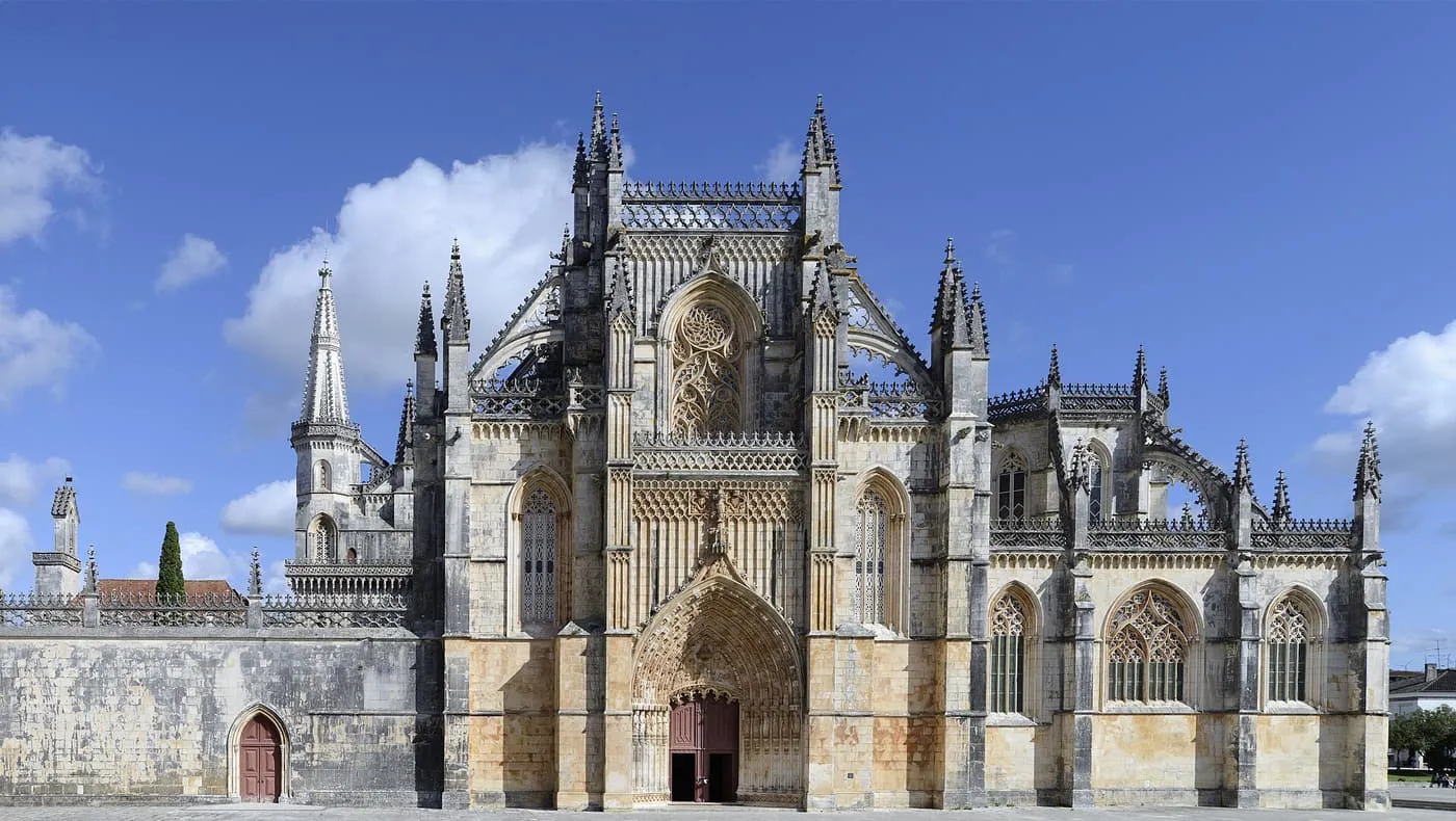 The Gothic front of Batalha Monastery, with pinnacles, tracery windows and a carved portal, under a blue sky