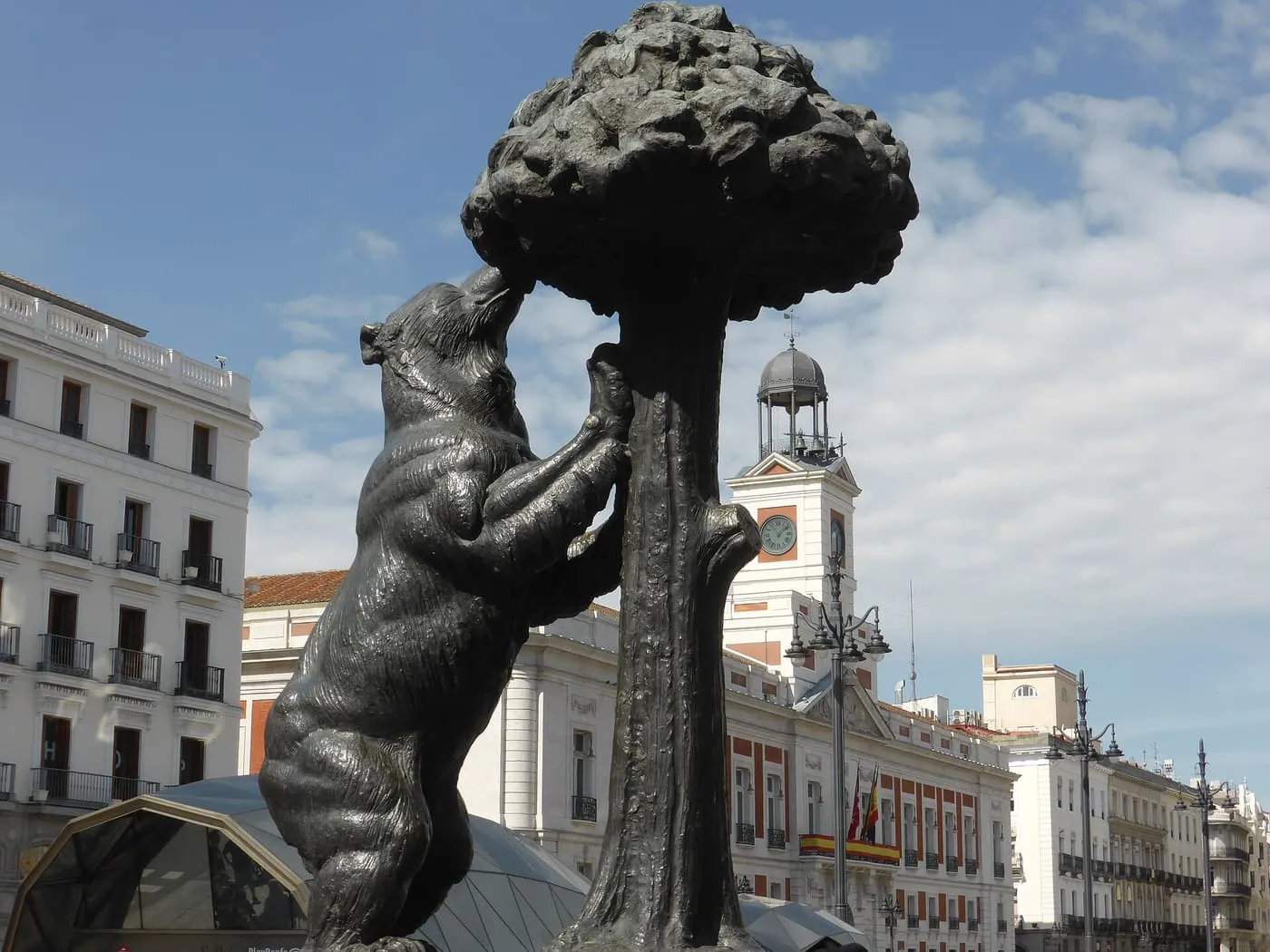 The bronze bear standing against the strawberry tree in the Puerta del Sol, with the Casa de Correos clock tower in the background