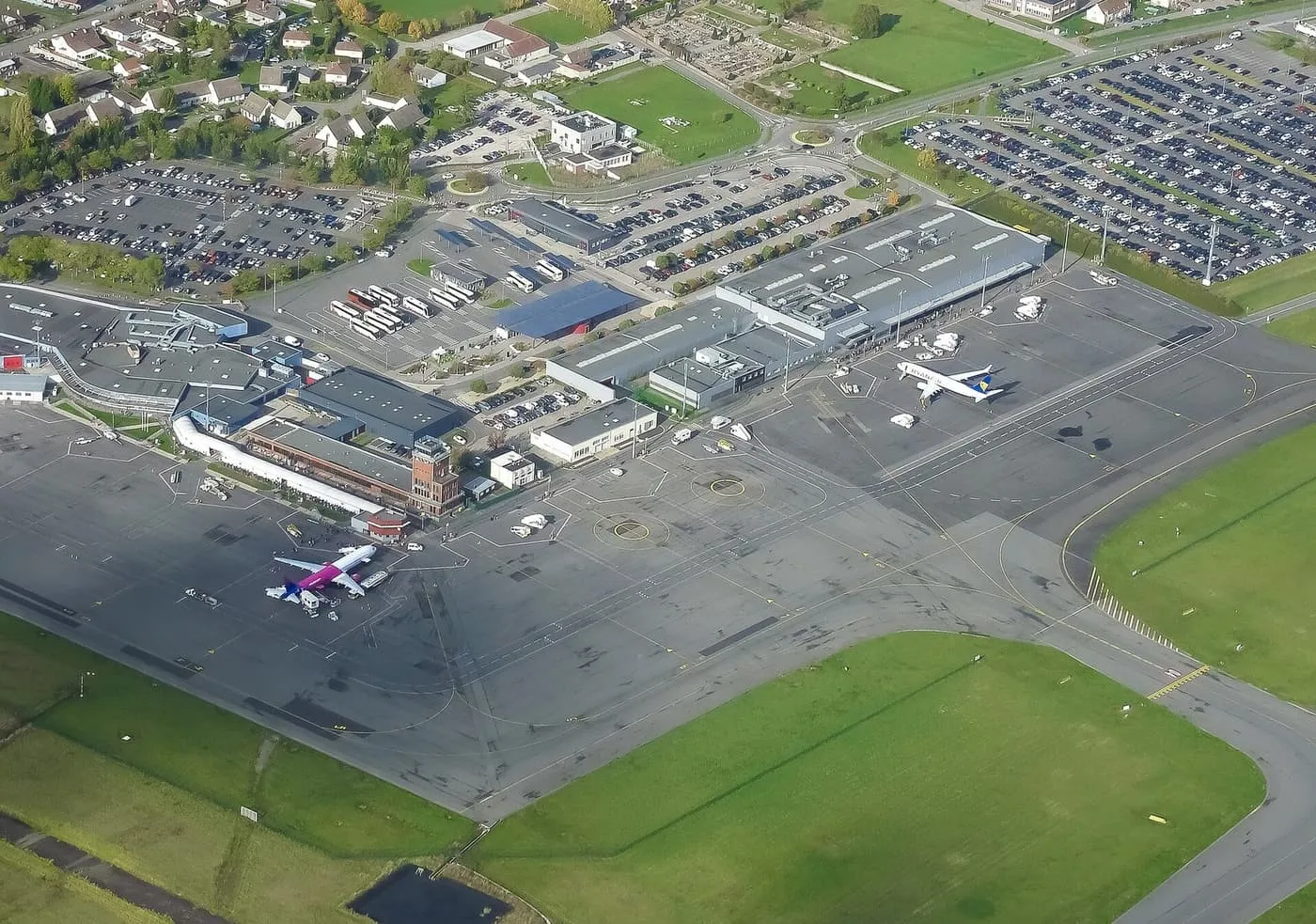 The terminal buildings of Beauvais airport seen from the air, with aircraft on the apron, a bus park and car parks around them