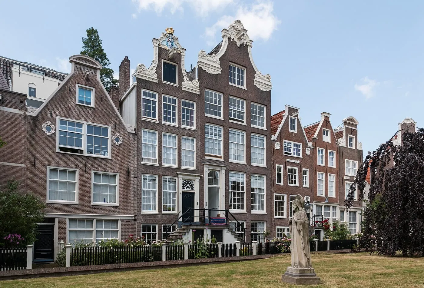 Tall brick houses with scrolled gables round the Begijnhof's lawn, with a stone statue in the foreground
