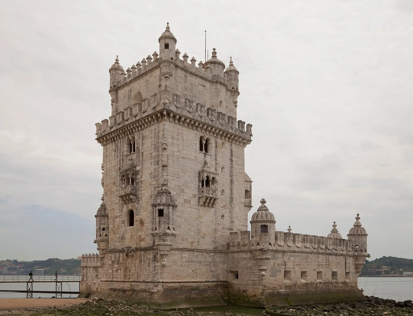 Belém Tower under an overcast sky, with a footbridge on its left