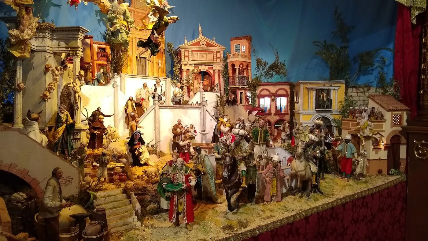 A large nativity scene of small figures among Andalusian-style buildings, with the Three Kings on horseback at the right and angels above
