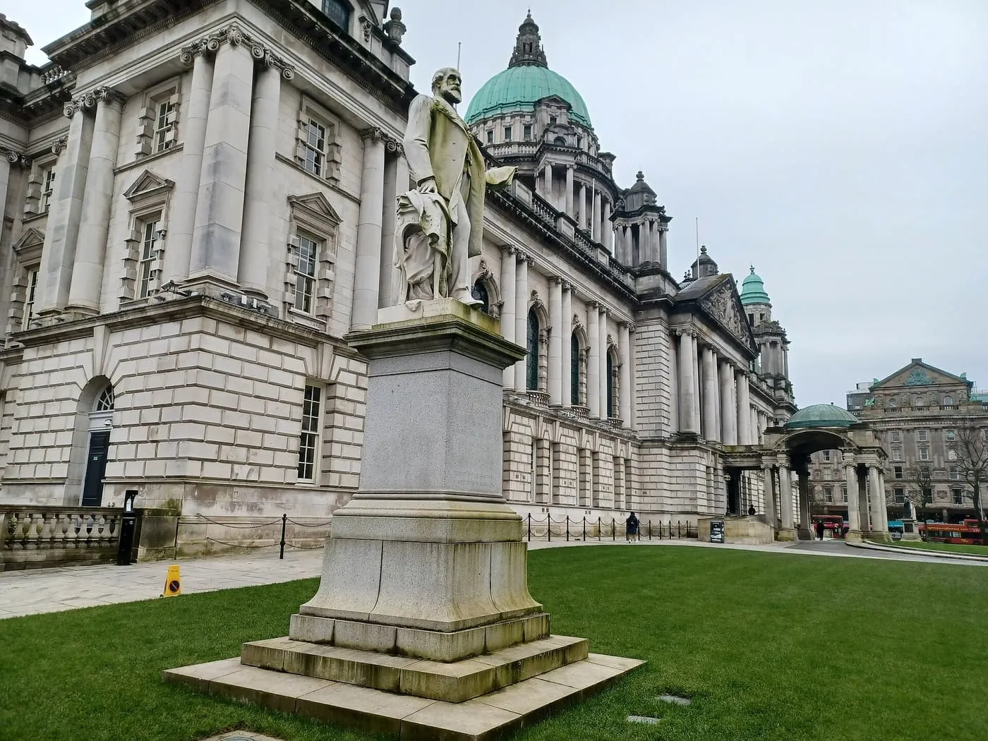 The stone front and green copper dome of Belfast City Hall, with a marble statue on a plinth in the foreground