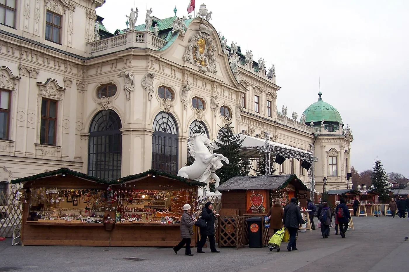 Wooden market huts selling decorations on the forecourt of the Belvedere, with a white rearing horse statue and the palace's green copper dome behind
