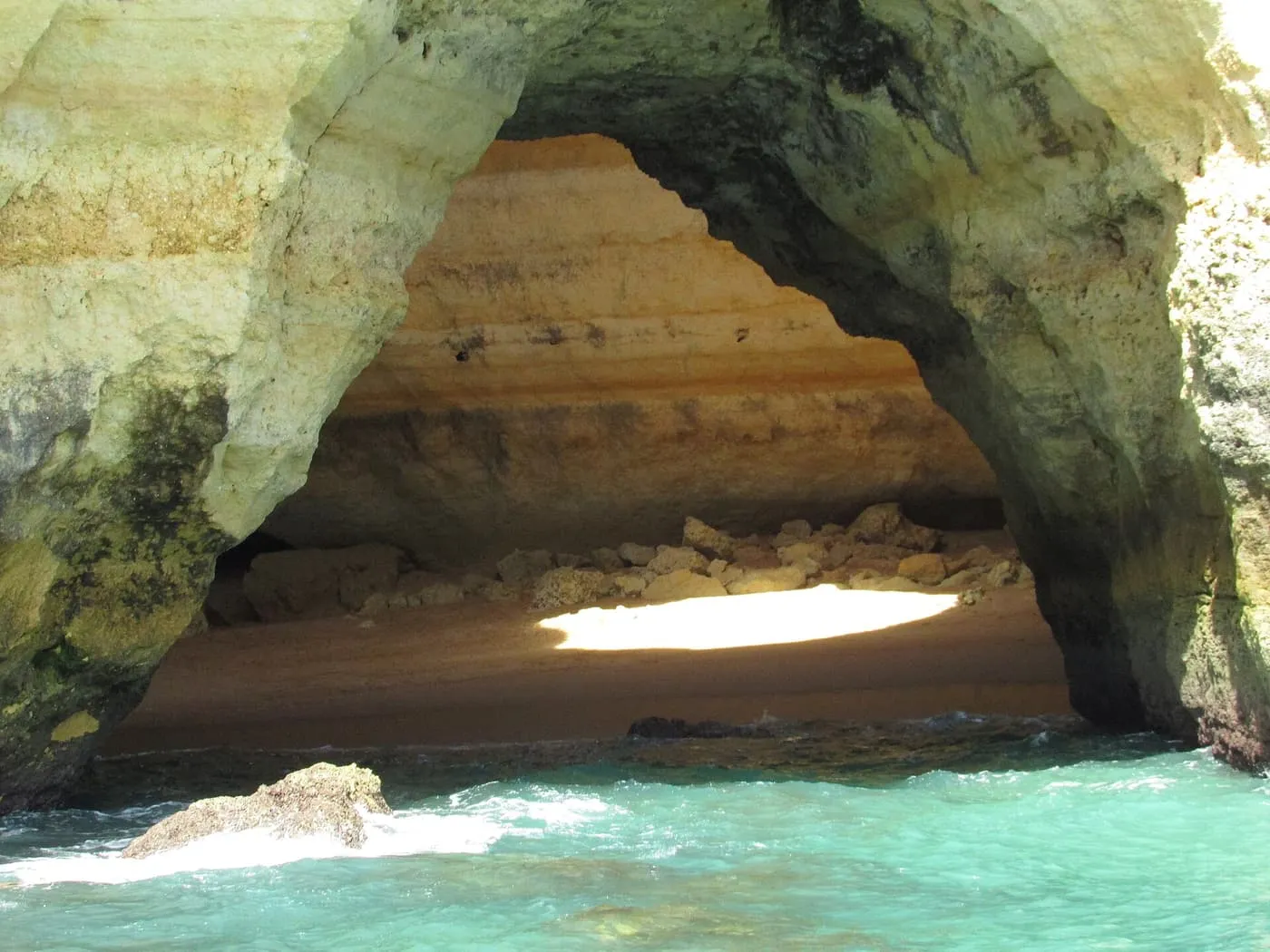 A sea cave on the Algarve coast near Benagil, seen from the water, with a patch of sunlight on its sandy floor