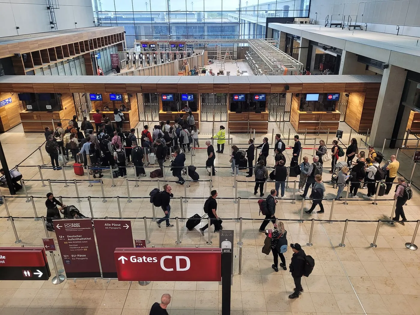 Passport control at Berlin Brandenburg Airport seen from above, with queues of travellers for the booths and signs for EU passports and all passports