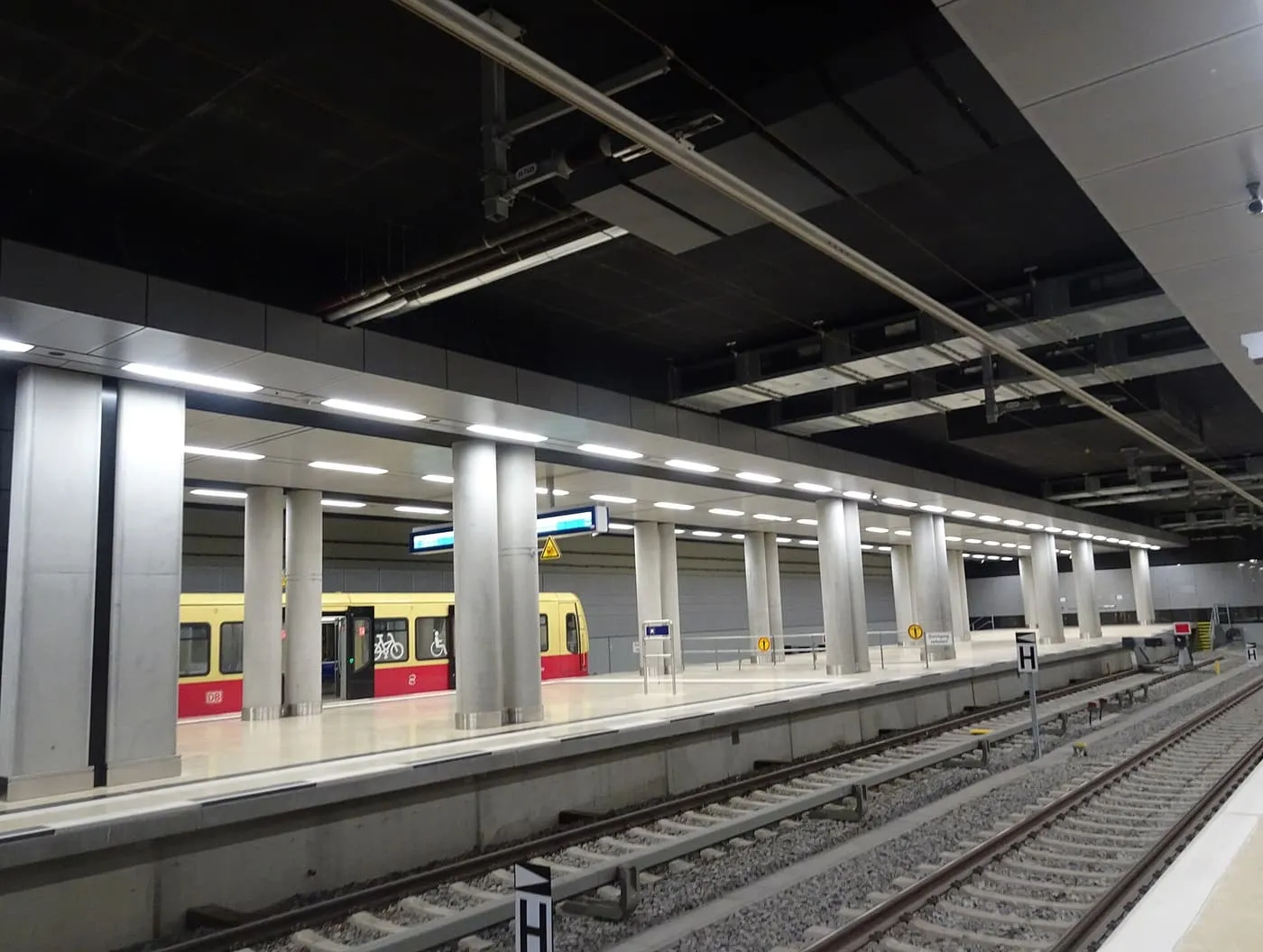 A red and yellow S-Bahn train at the concrete-pillared S-Bahn platform of the BER station