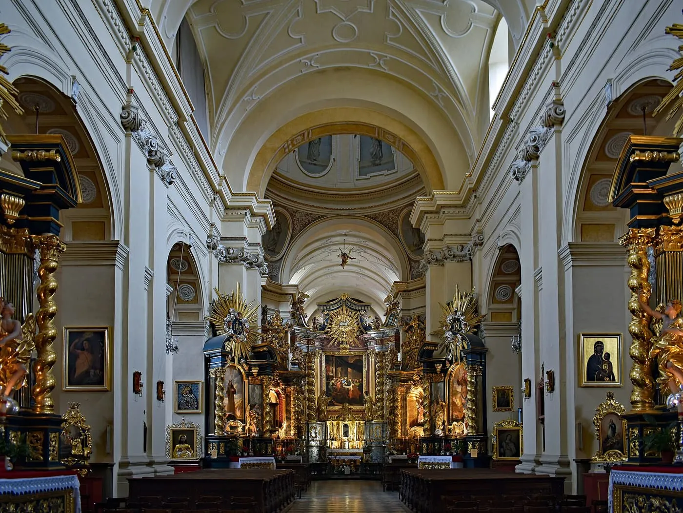 The nave of a baroque church, with white and gold walls, twisted gilded columns and a high altar at the far end