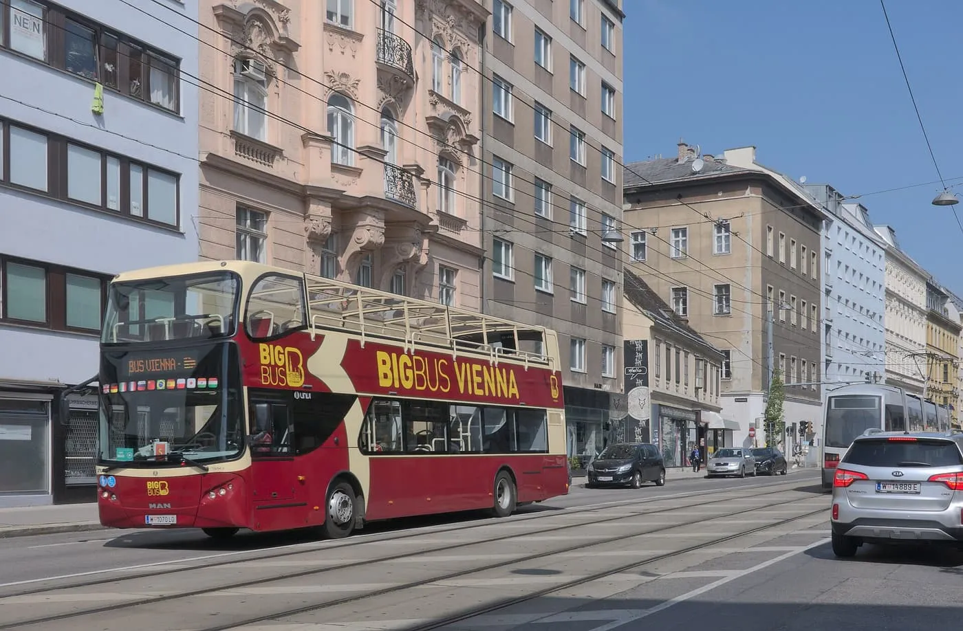 A red and cream open-top Big Bus Vienna double-decker on a street of apartment buildings