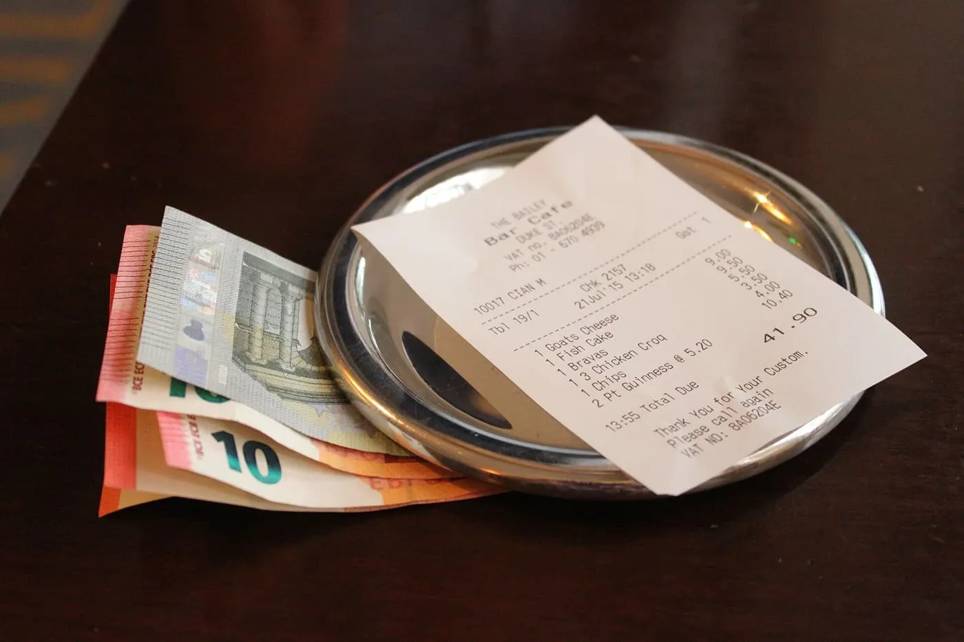 A paper bill and euro notes lying on a small metal tray on a table