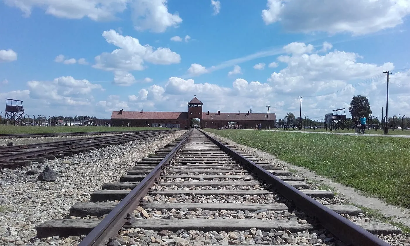 The railway line running across a field to the gatehouse at Auschwitz II-Birkenau under a partly cloudy sky