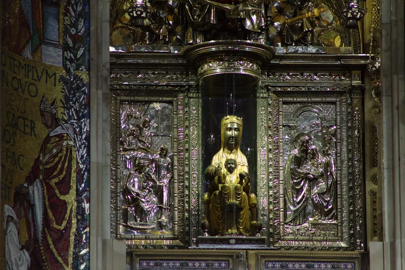 The dark-faced gilded statue of the Virgin and Child in a glass niche, framed by silver relief panels