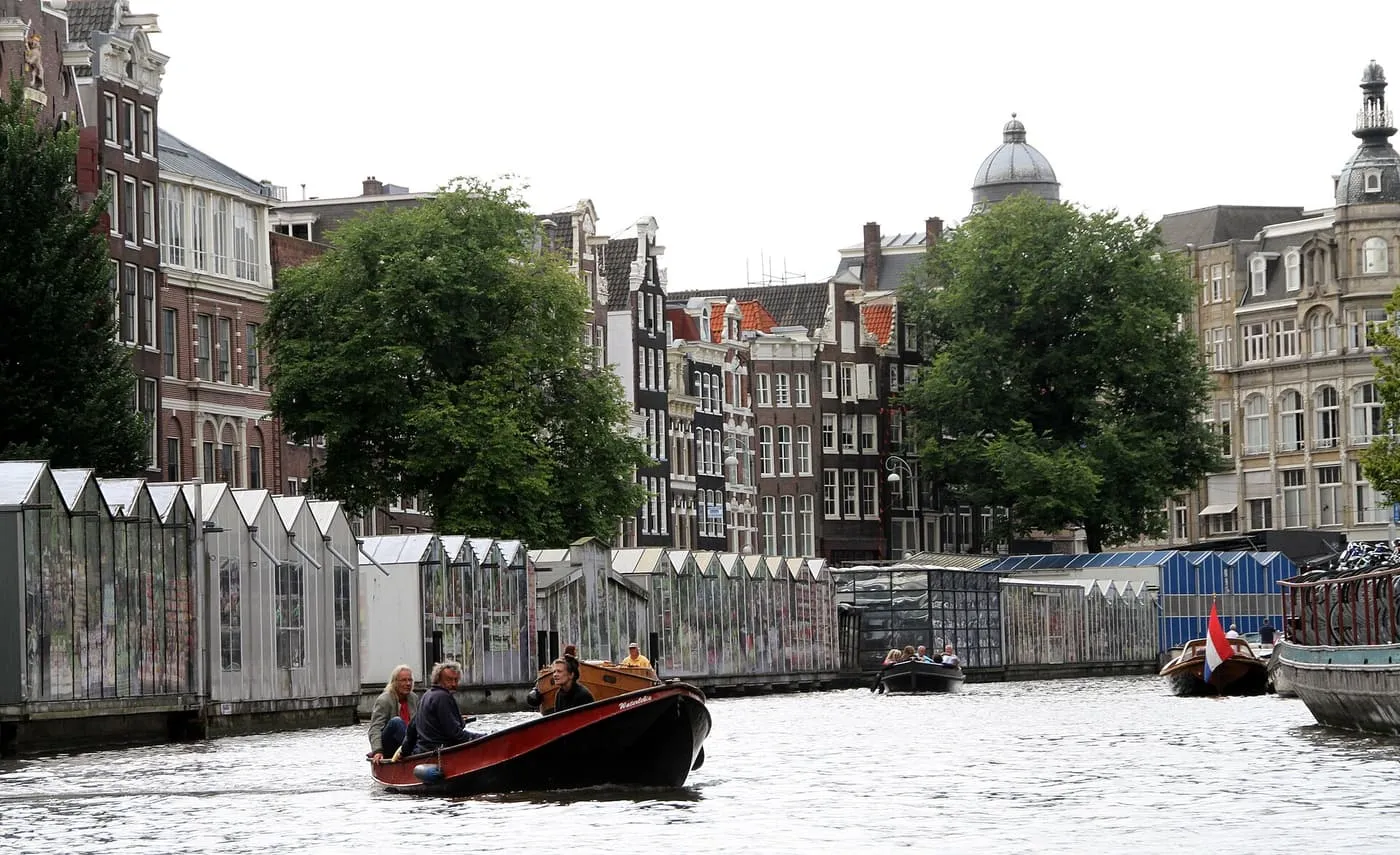 Greenhouse-style flower stalls moored along the Singel, with small boats on the canal and gabled houses behind