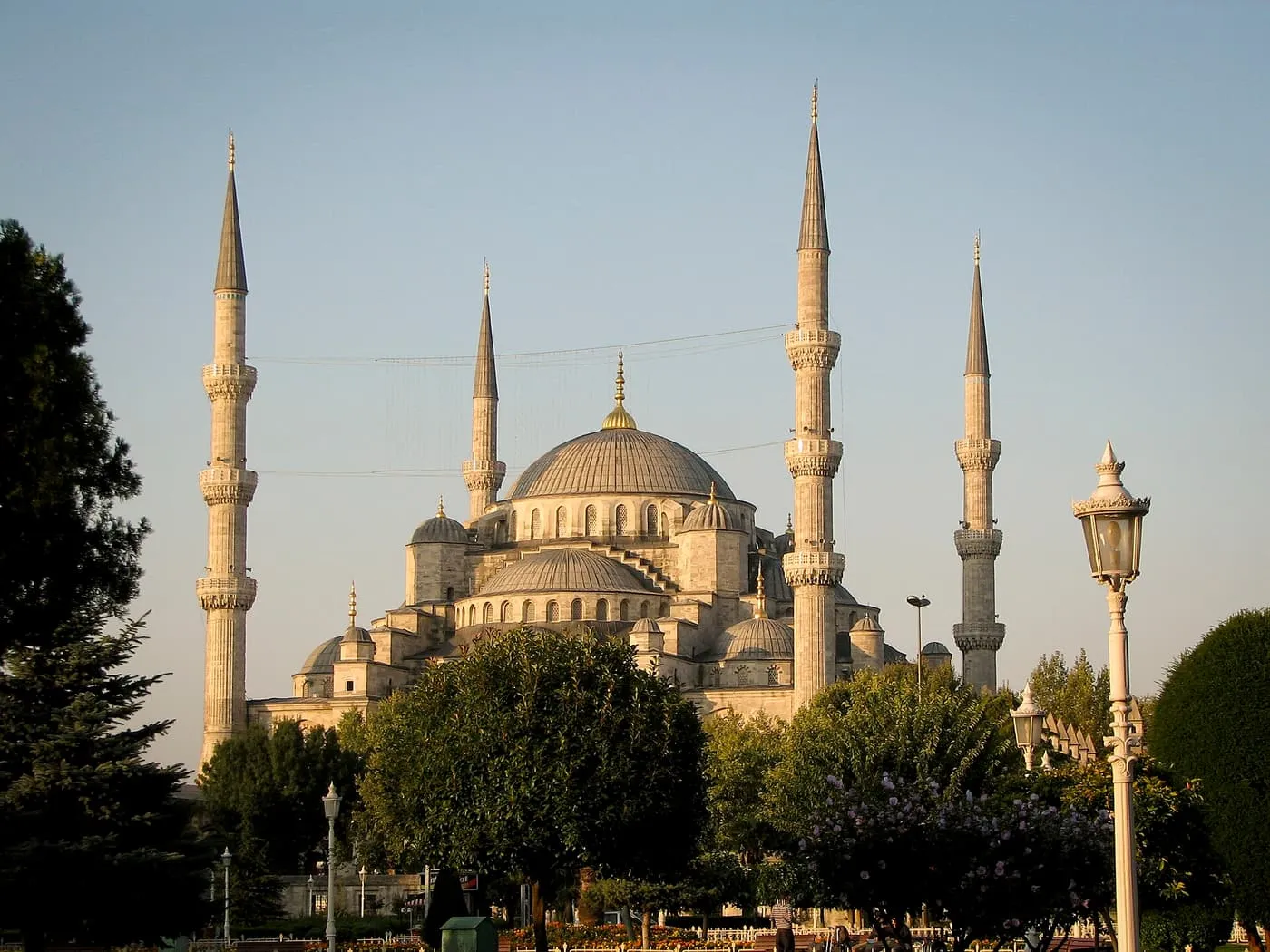 The Blue Mosque's central dome and four of its minarets, lit gold by low sun above trees and lamp posts