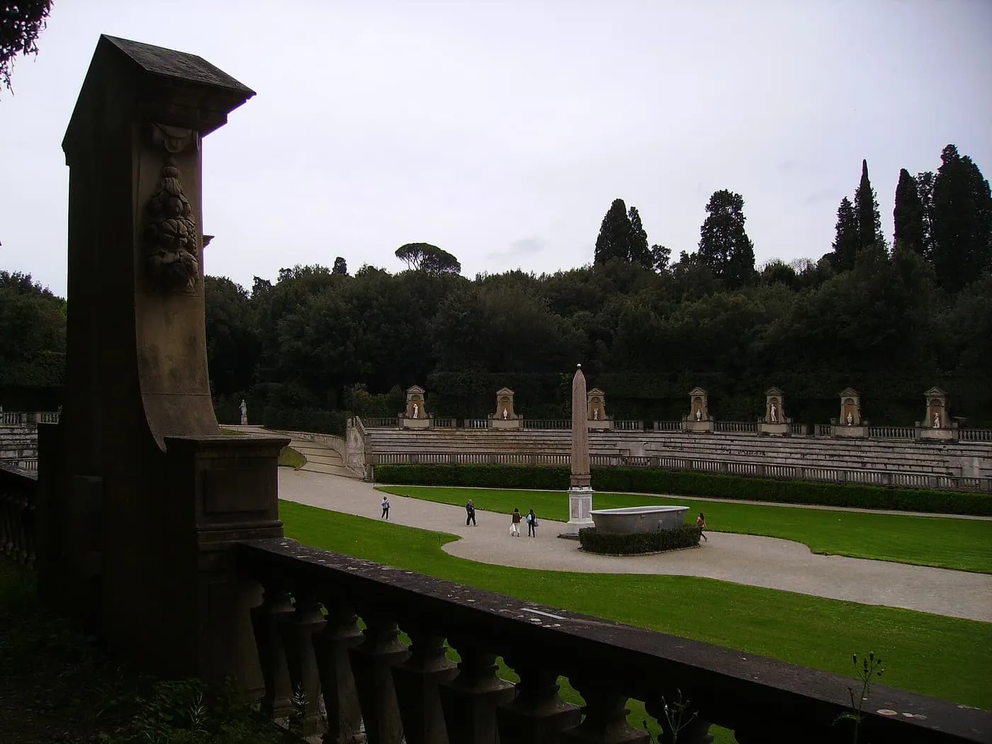 The amphitheatre of the Boboli Gardens seen over a stone balustrade, with an obelisk and a lawn in front of its stepped seating