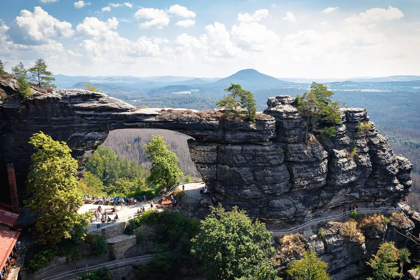 Pravčická brána, a sandstone arch in Bohemian Switzerland, with forest beyond it and a viewing terrace with visitors below