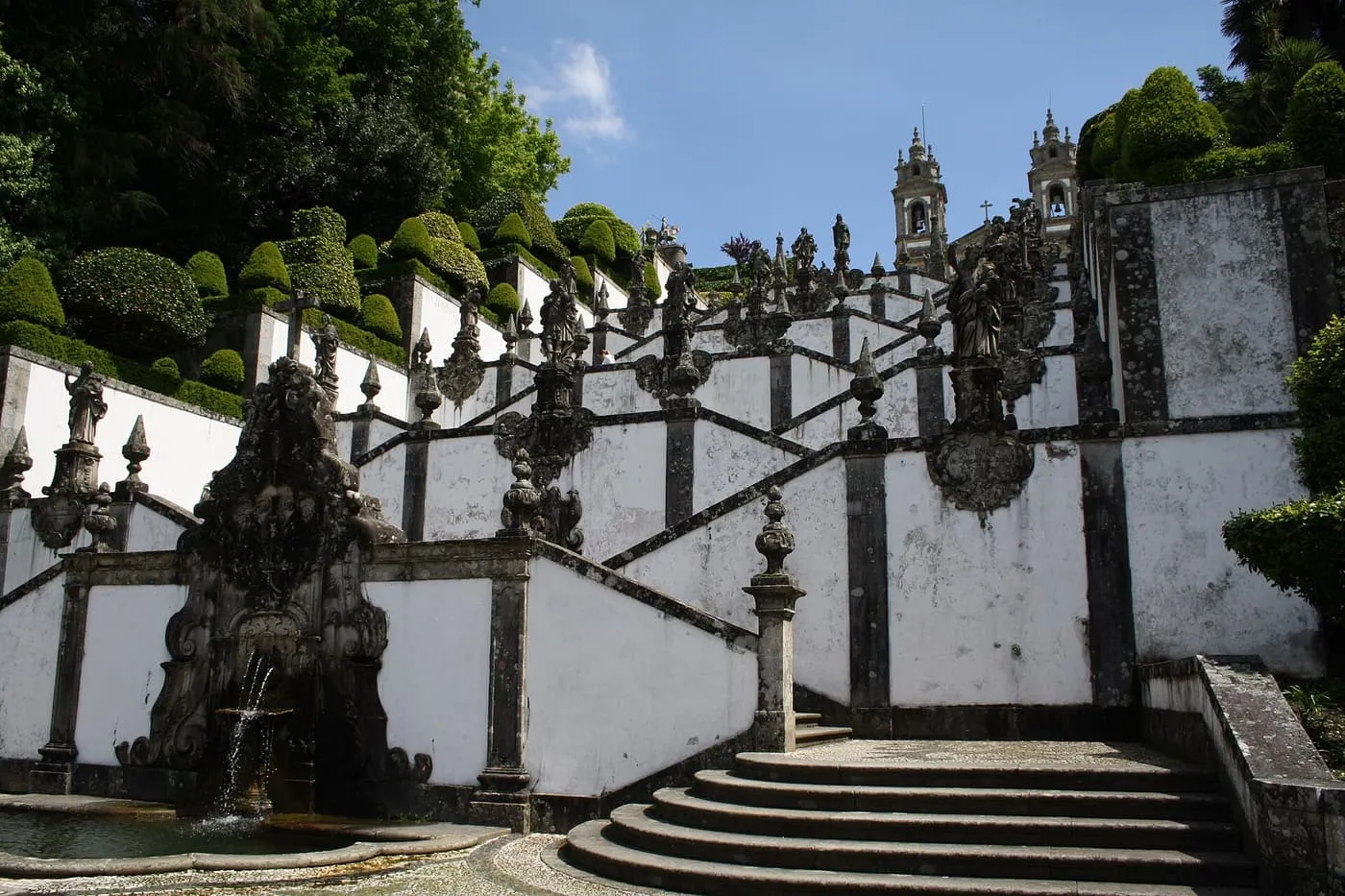 The white zigzag stairway of Bom Jesus do Monte, with granite statues, clipped hedges and a fountain at the foot, and the church towers at the top