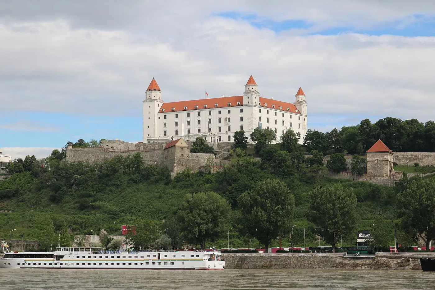 The white four-towered Bratislava Castle on its hill above the Danube, with a river boat in front