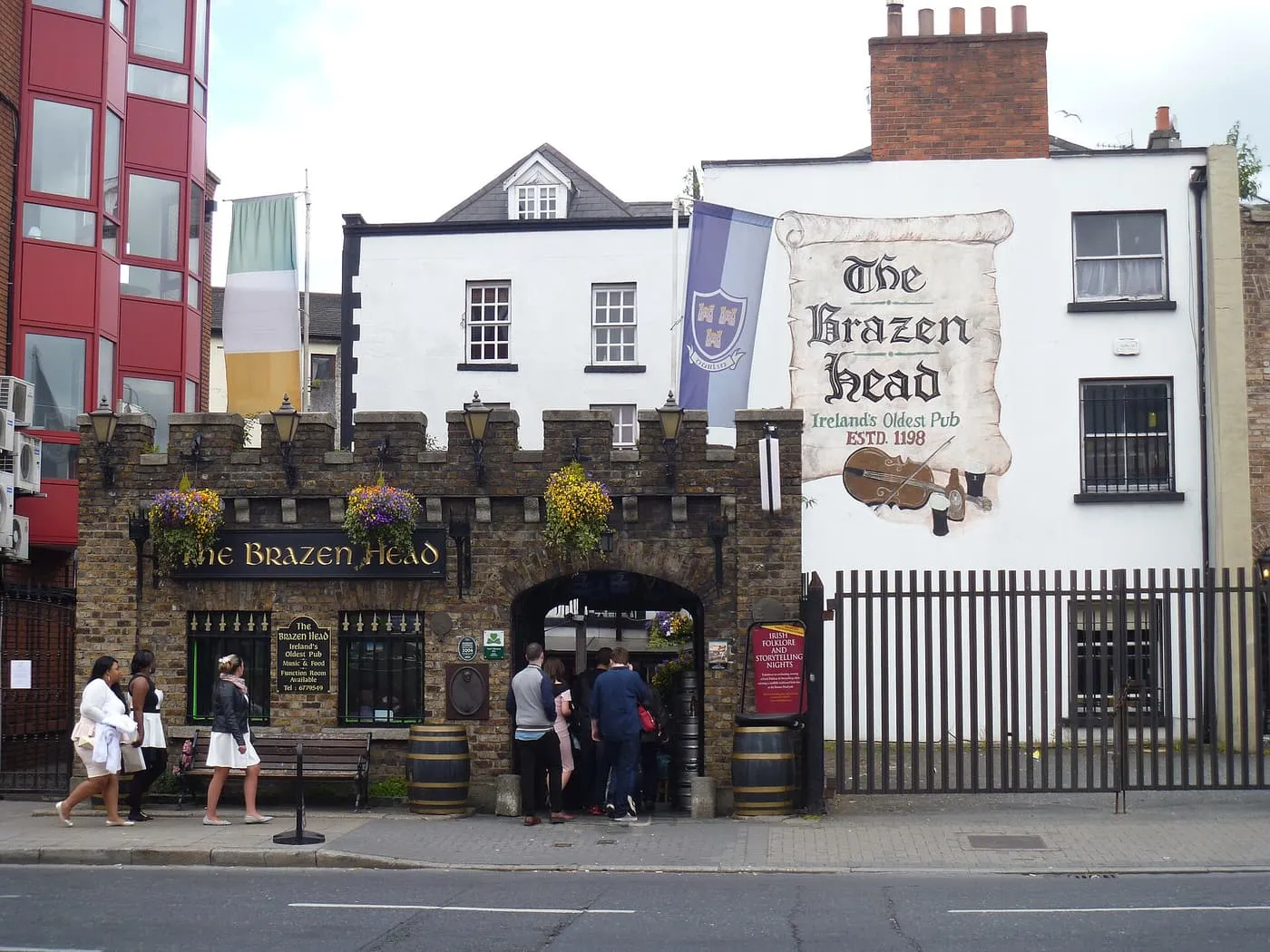 The crenellated stone front of the Brazen Head pub beside a white gable painted with its name and 'Ireland's Oldest Pub, estd 1198'
