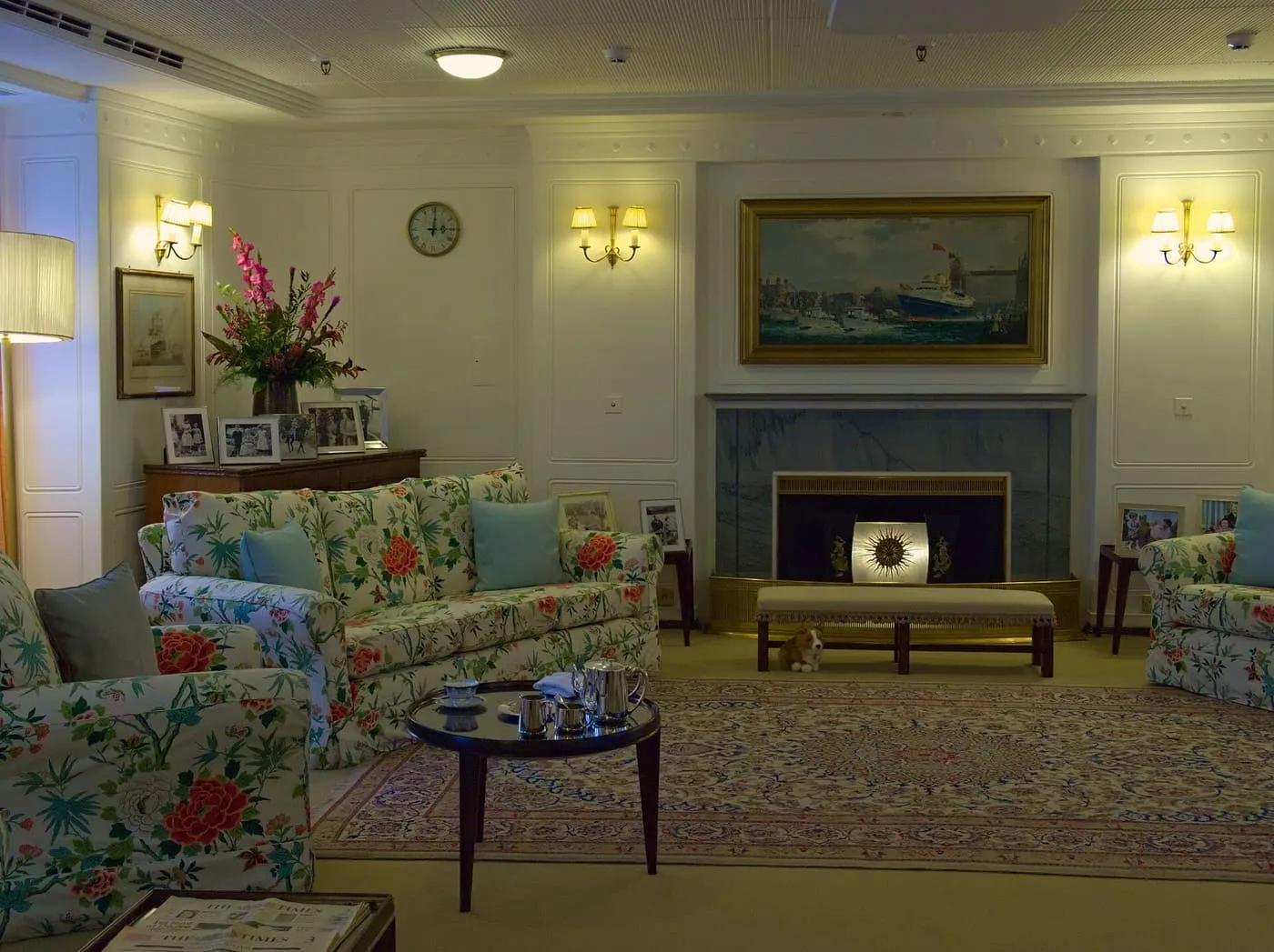 A sitting room with floral sofas, a marble fireplace and a painting of the yacht above it