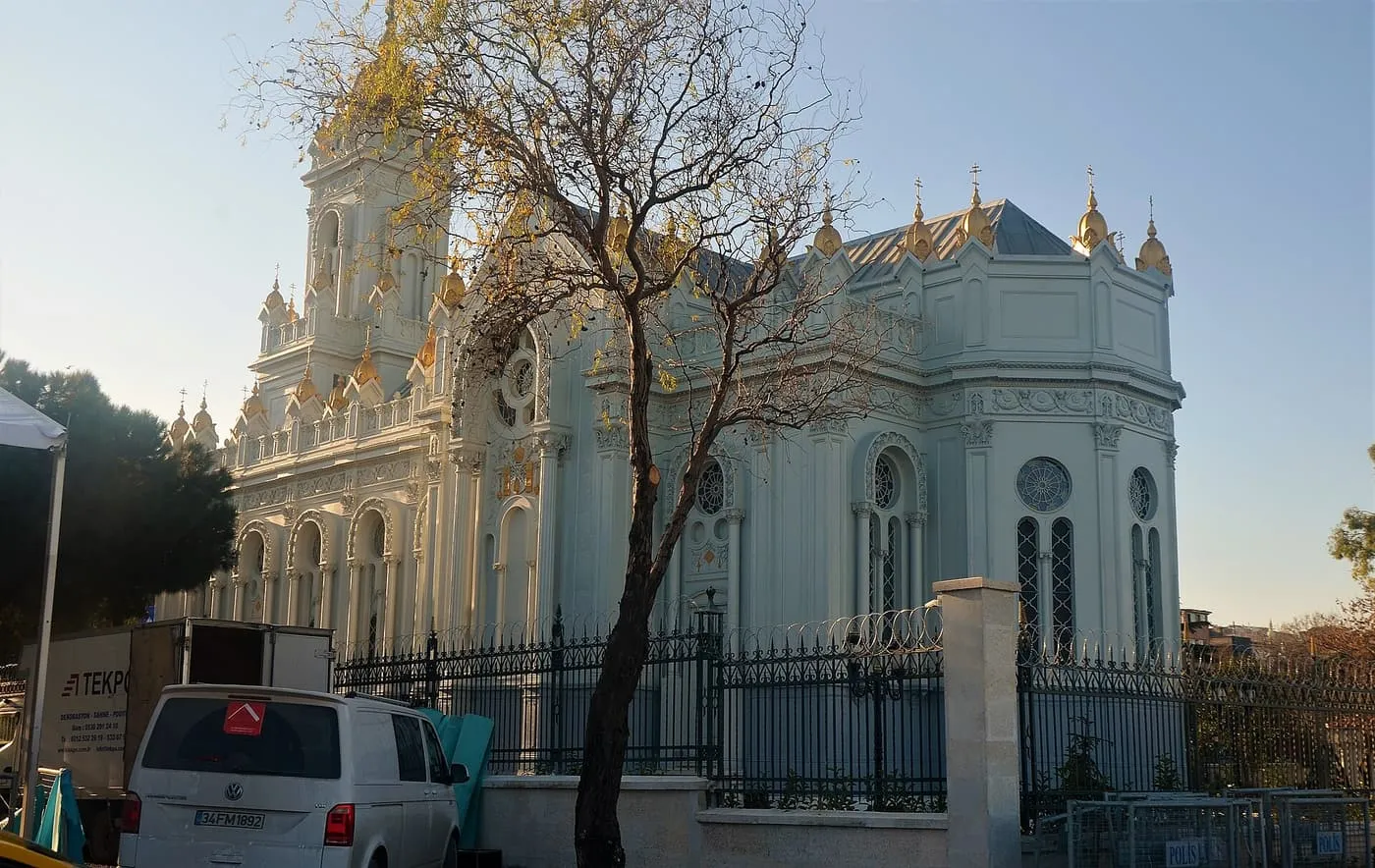 The pale blue-green Bulgarian St Stephen Church in Fener, an iron-framed building with gilded domes, behind black railings and a bare tree
