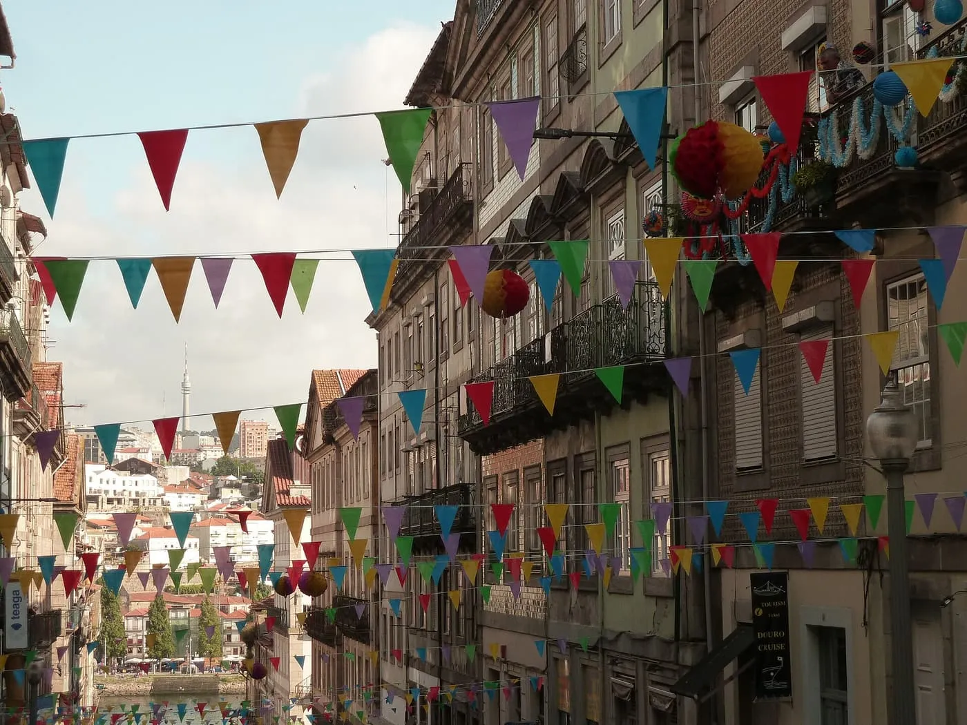 A steep street of old houses hung with rows of coloured paper bunting and lanterns, running down towards the river