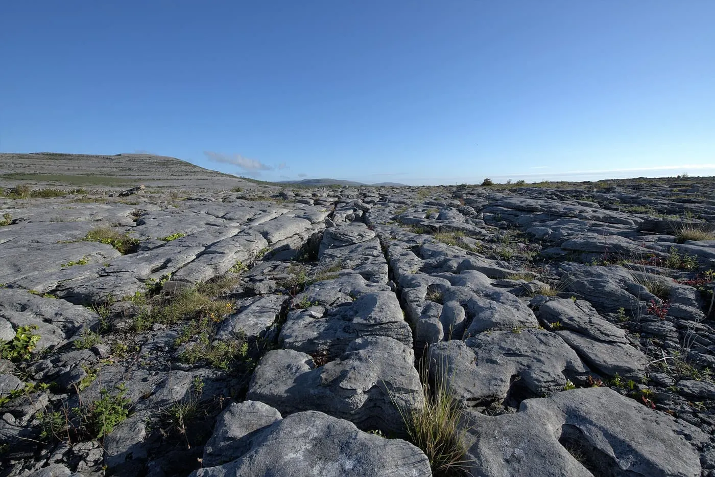 Grey limestone pavement split into slabs by deep cracks on a Burren hillside under a clear sky